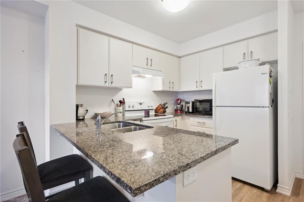 Kitchen featuring a peninsula, white appliances, a kitchen bar, white cabinetry, and dark stone counters