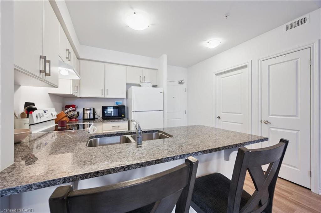 Kitchen featuring a peninsula, a kitchen breakfast bar, white appliances, white cabinetry, and light wood-type flooring