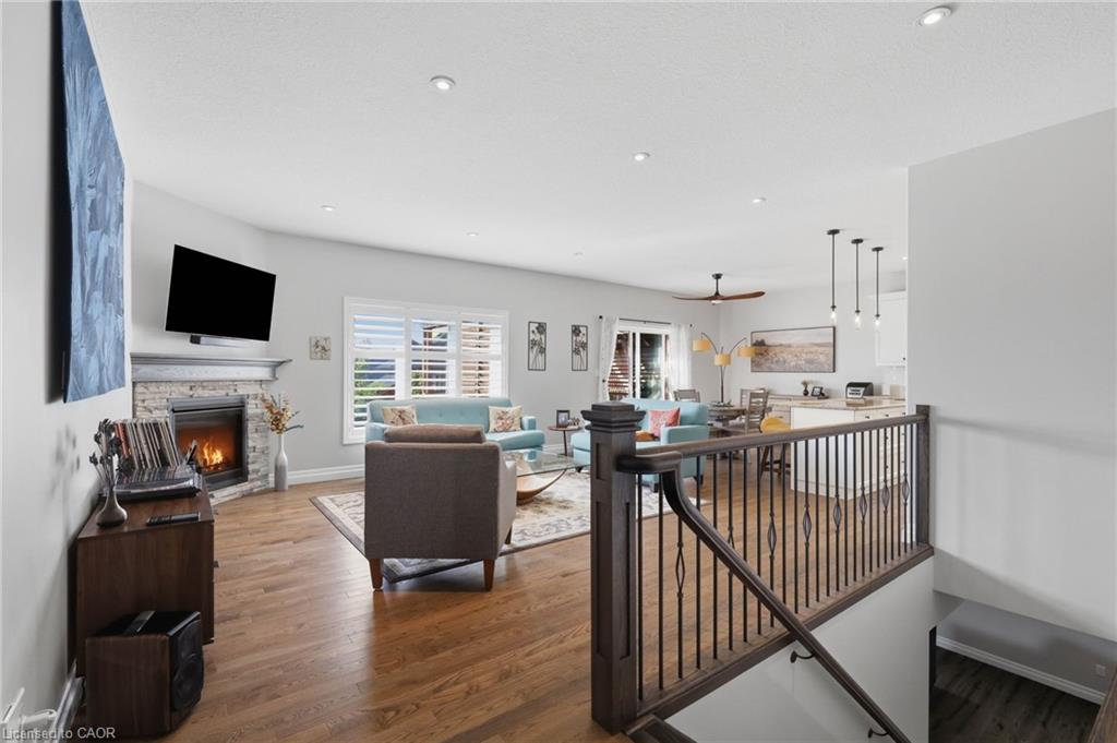 Hardwood-finish flooring, stone-clad fireplace, plantation shutters, recessed lighting, and a dark wood and iron-spindle railing system