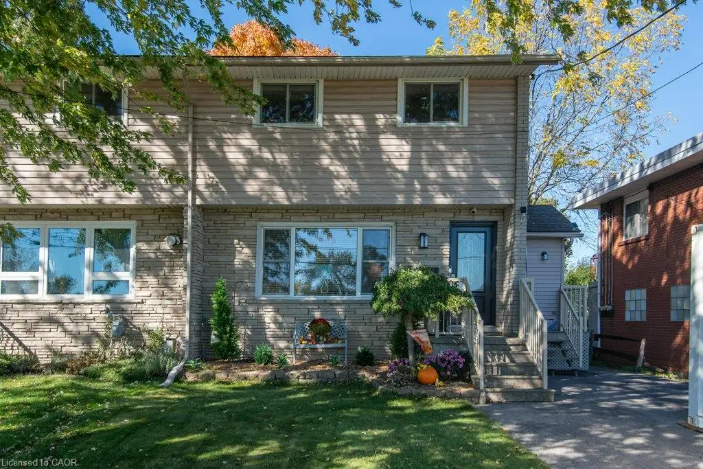 Multi-level exterior featuring light-toned horizontal siding, lower-level stone facade, multi-pane windows, and concrete front steps with metal railing