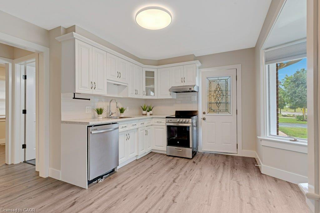 Bright kitchen featuring white shaker cabinetry, stainless steel appliances, light wood-finish flooring, a decorative glass paneled exterior door, and a bay window