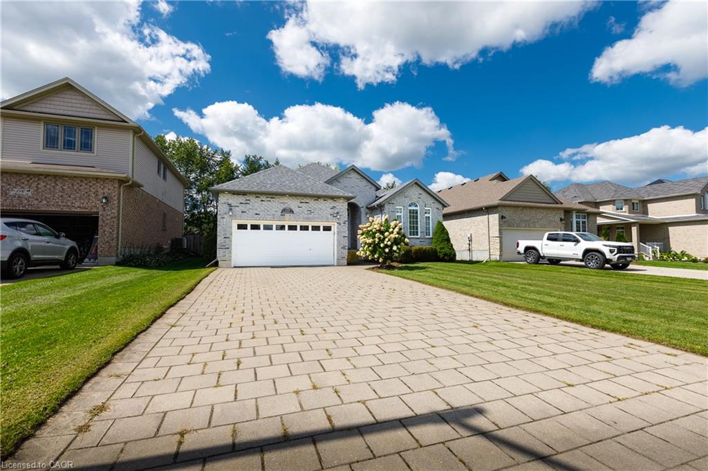 Paver driveway with a two-car garage, stone and siding exterior, and landscaped lawn
