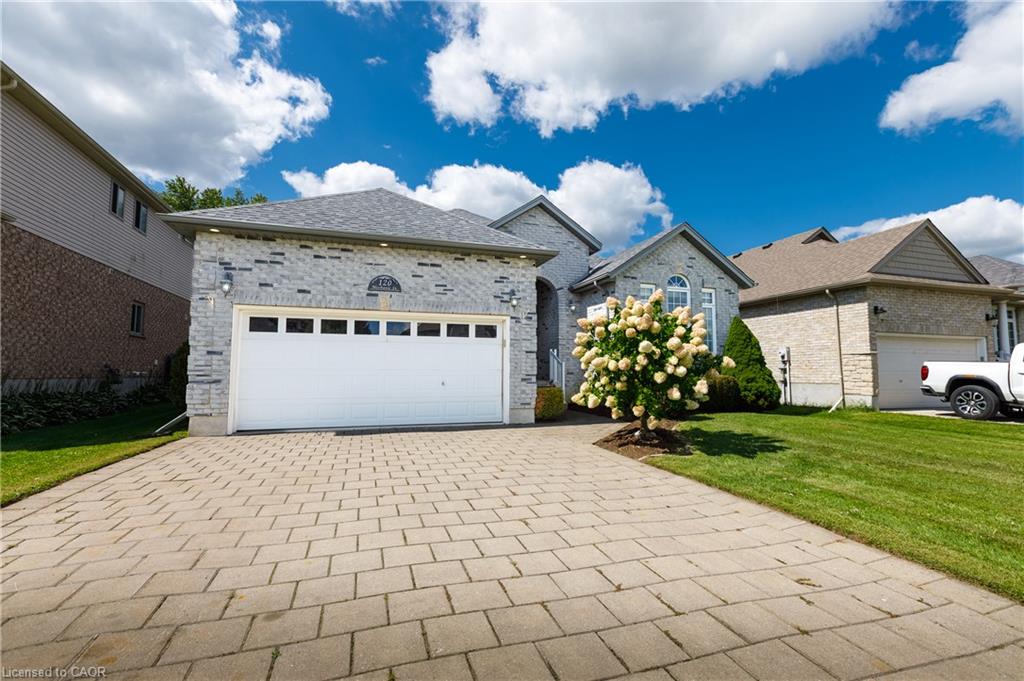 Stone and brick exterior with an attached garage, paver driveway, and manicured lawn