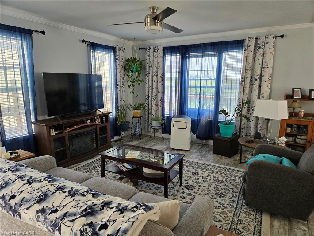 Living area with bay windows, wood-finish flooring, and crown molding