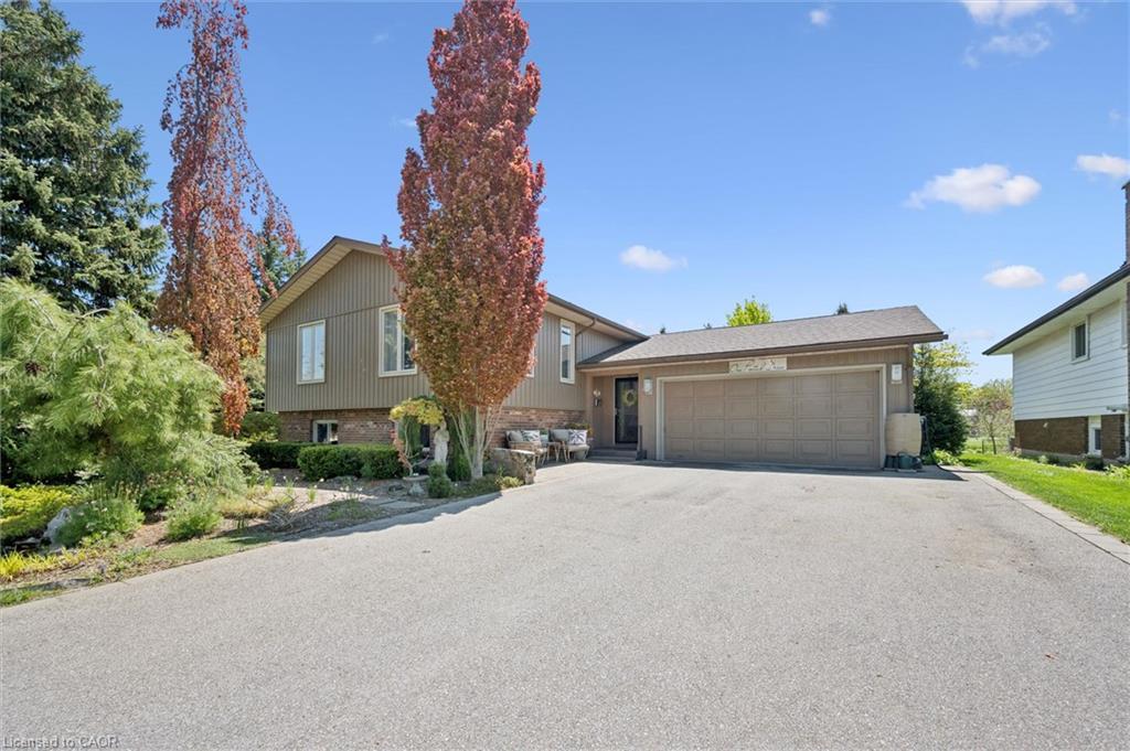 Split-level residence featuring a two-car garage, mature trees, and landscaped garden beds