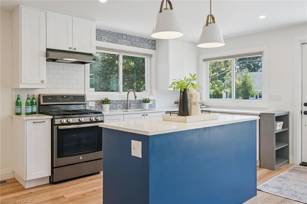 Kitchen featuring a central island with countertop, stainless steel range, white cabinetry, wood-finish flooring, and pendant lighting