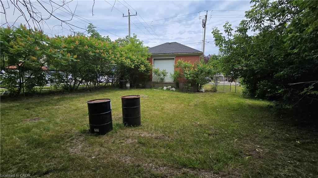 Expansive grassy yard area featuring mature shrubbery and a brick-sided structure with a roll-up door and dark shingle roof
