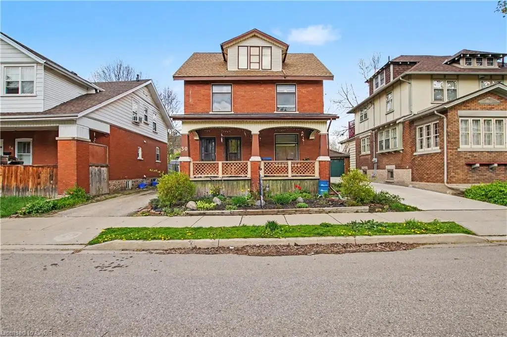 Red brick facade residence featuring a covered front porch with decorative railing, dormer window, and a planted front garden bed