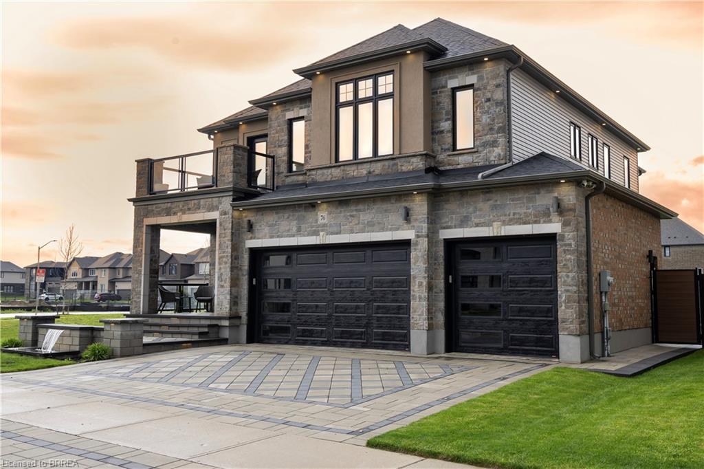 Stone and brick exterior with a multi-car garage featuring modern doors, a covered patio, and a second-story balcony with glass railings