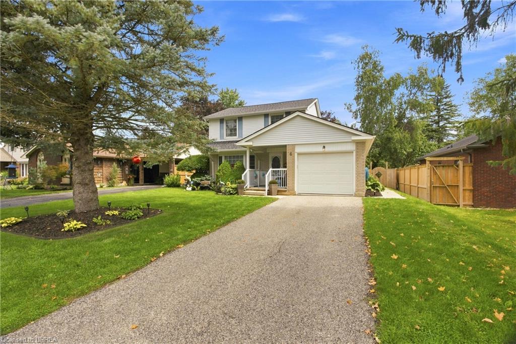 Two-story siding and brick exterior with attached garage, paved driveway, and manicured front lawn featuring a mature tree
