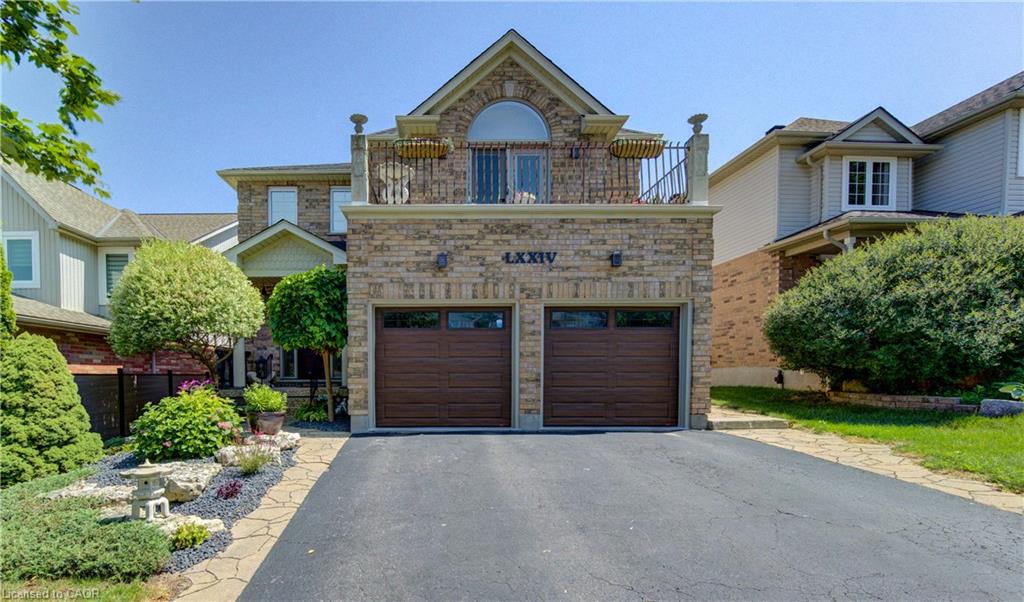 Stone facade home featuring a two-car garage with wood-finish doors, an upper-level balcony with a wrought iron railing, and an arched window