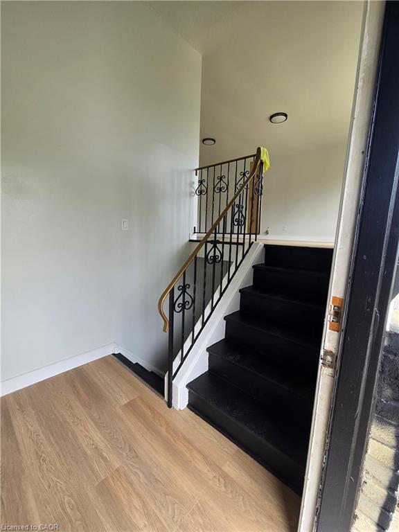 Wood-finish flooring with white baseboards, black-painted staircase, black wrought iron railing with wood handrail, and recessed ceiling lighting