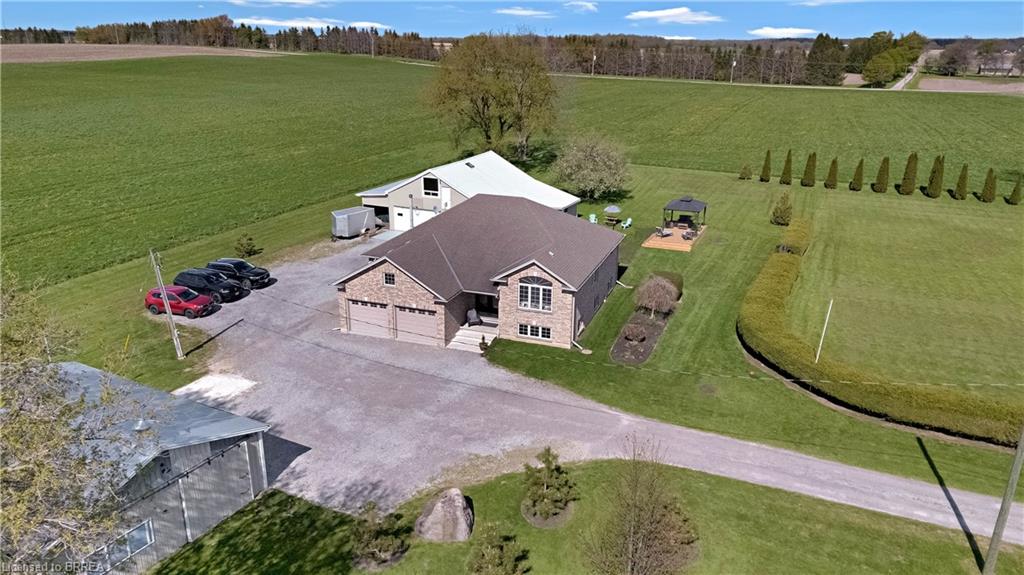Spacious property featuring a brick and siding residence with an attached double garage, a large detached outbuilding, extensive gravel driveway, and a backyard gazebo with a stone patio