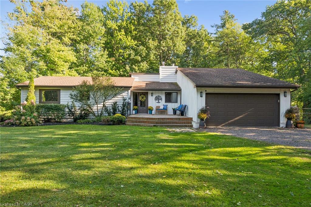 Expansive front lawn, mature trees, wood-finish front porch, attached garage with dark door, and white exterior siding
