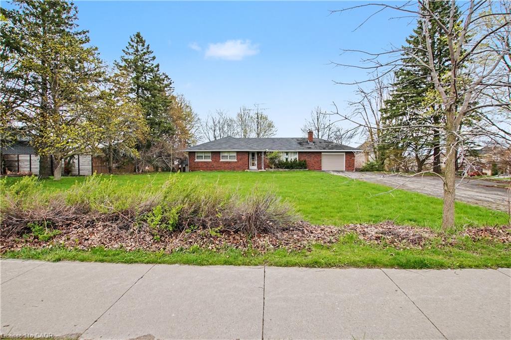 Brick ranch-style residence featuring an attached garage, a paved driveway, and a spacious front lawn