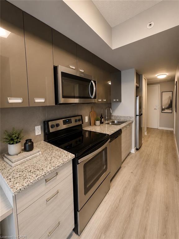 Contemporary kitchen featuring stainless steel appliances, speckled countertops, gray-toned flat-panel cabinetry, and wood-finish flooring