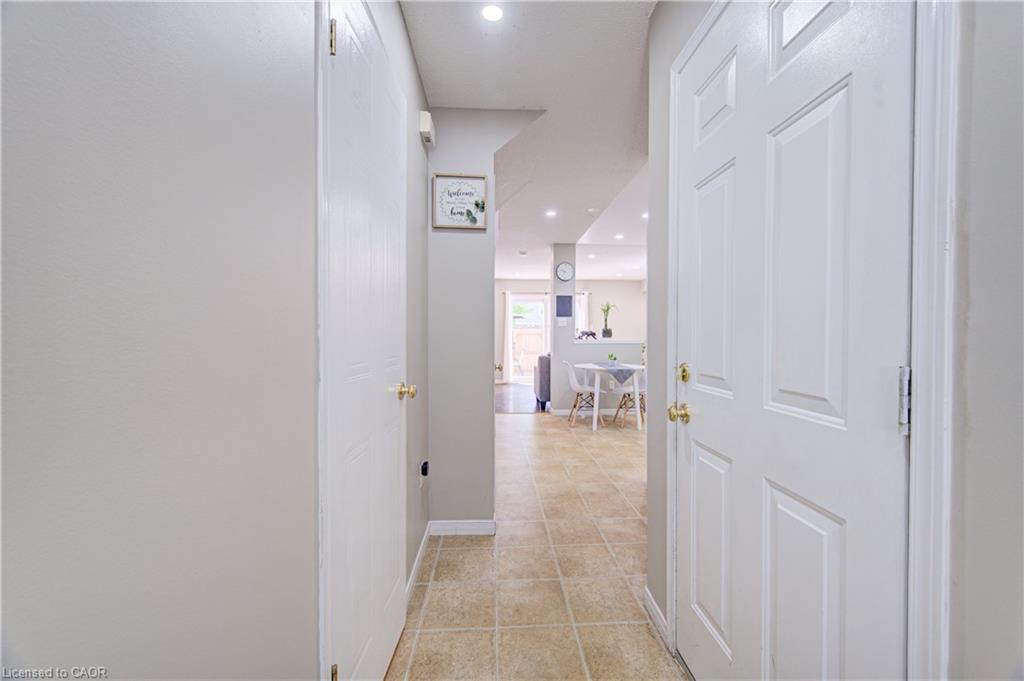 Recessed lighting illuminates the hallway with light-toned walls and paneled doors, complemented by brass door hardware and square-tiled flooring