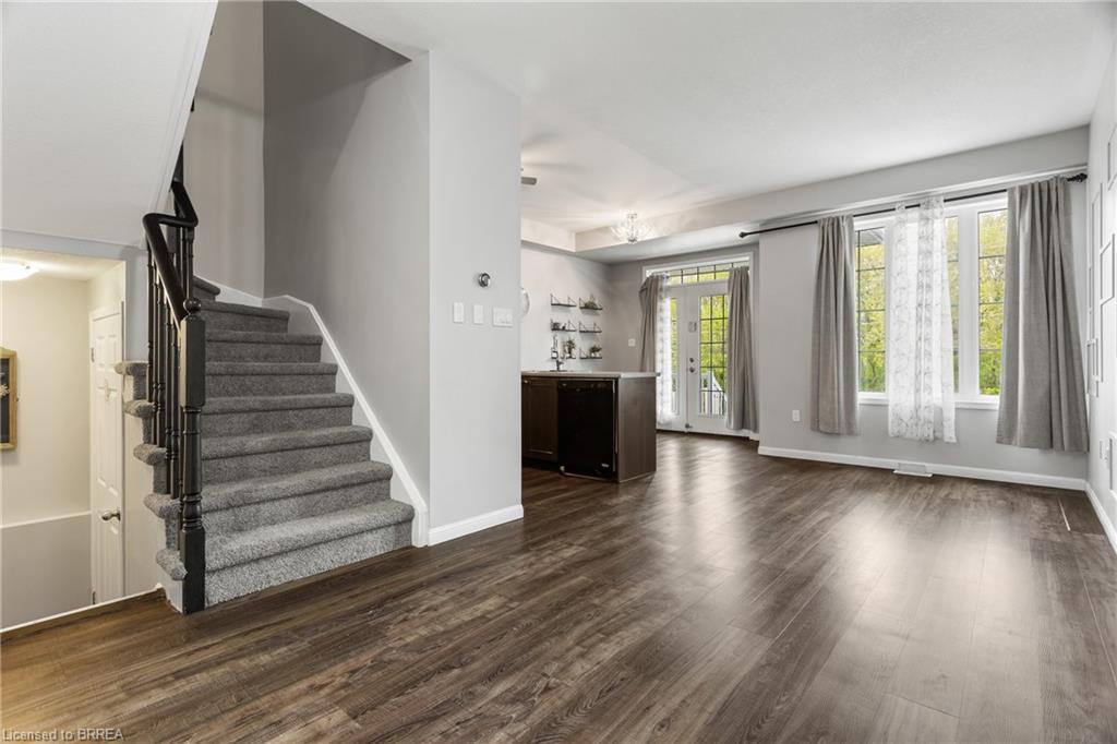 Open-concept living area featuring rich wood-finish flooring, a large window with white trim, and a glass-paneled exterior door