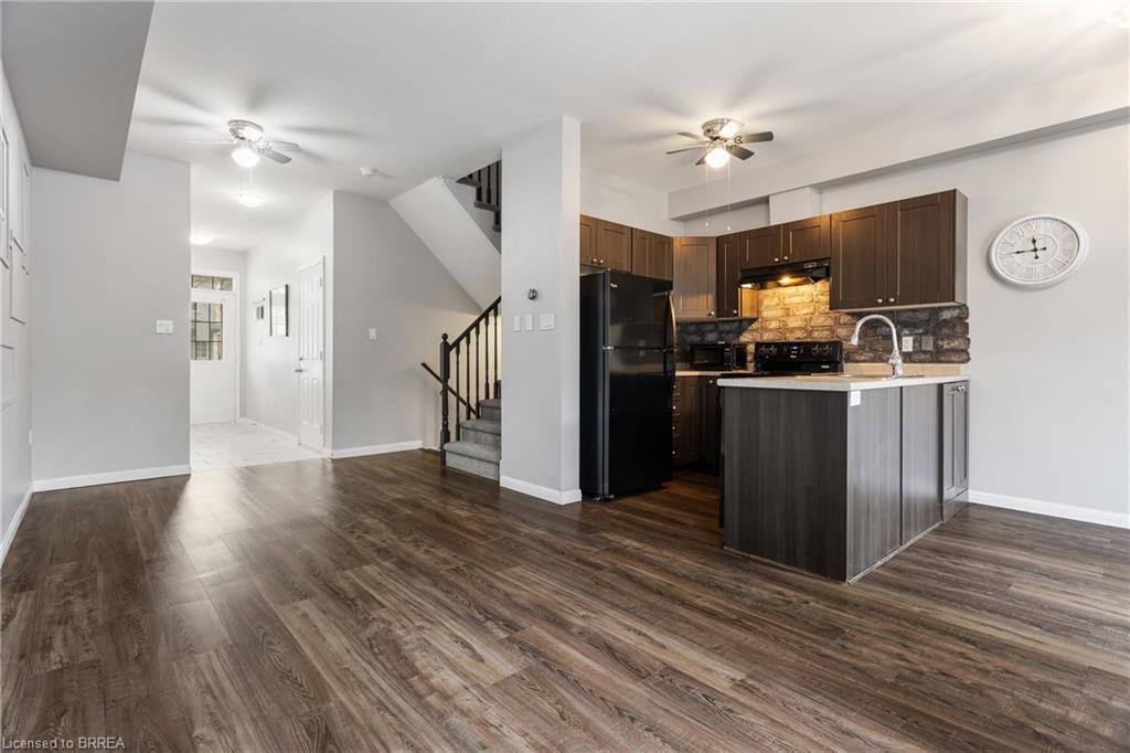 Open-concept main level featuring wood-finish flooring, a kitchen island with integrated sink, dark wood cabinetry, and a stone-finish backsplash