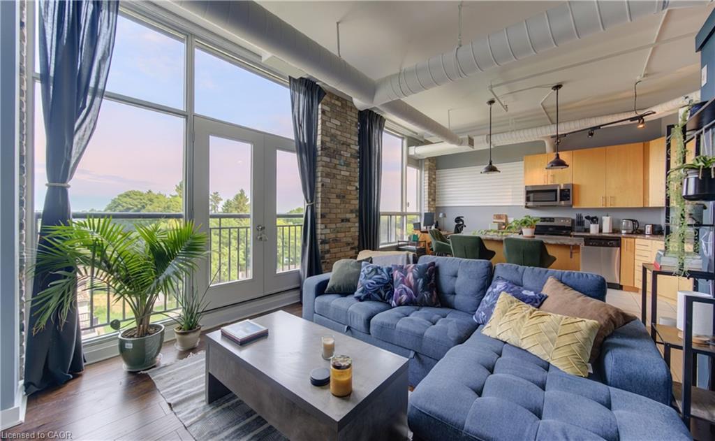 Expansive floor-to-ceiling windows with balcony access, featuring dark wood-finish flooring, exposed brick accents, and visible ductwork