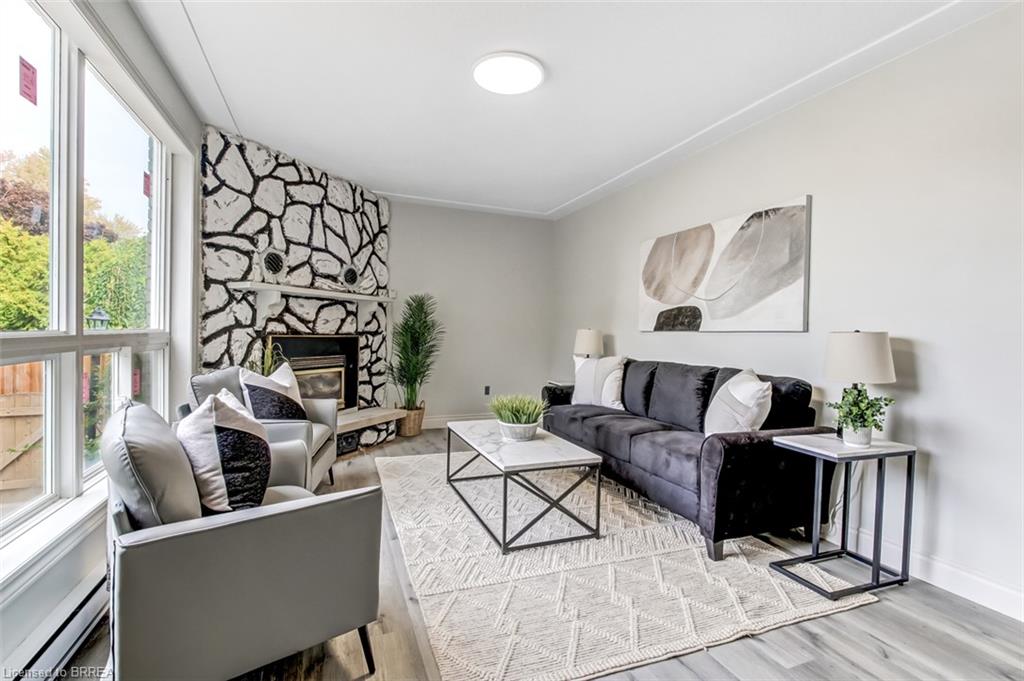 Living area featuring a stone accent wall with a built-in fireplace, large picture windows, wood-finish flooring, and crown molding