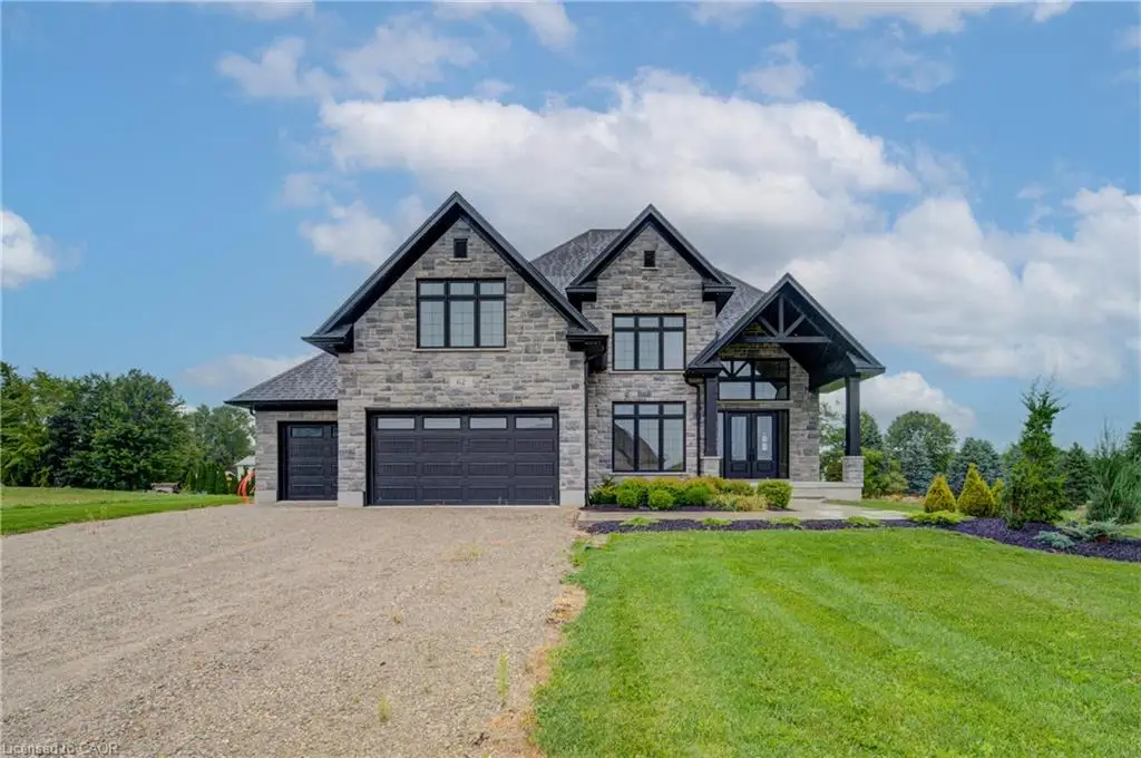 Stone facade residence with prominent gables and a covered entry, featuring large black-framed windows and multiple garage doors