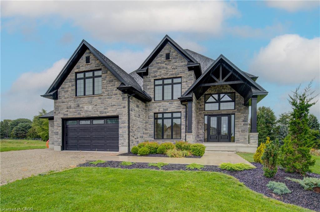 Stone exterior with gabled roof lines, featuring a double-door entry with transom window, an attached two-car garage, and established front landscaping