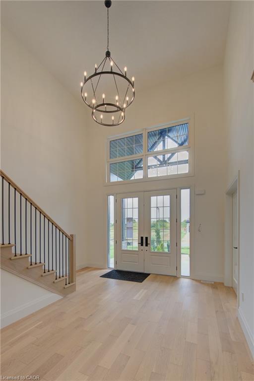 Double-height entryway featuring a tiered chandelier, wood-finish flooring, and a staircase with metal balusters