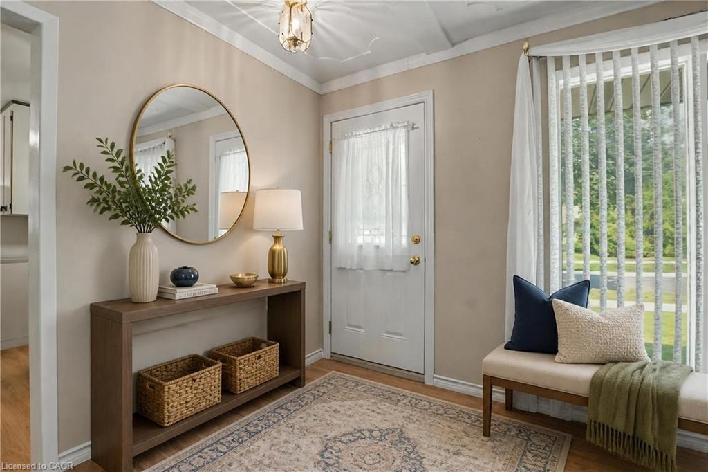 Wood-finish flooring, overhead decorative lighting fixture, front door with transom window, and a window with vertical blinds