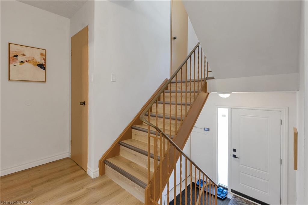 Staircase with wood-finish treads and railing, white paneled door, and wood-finish flooring