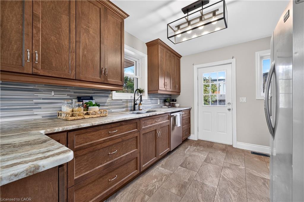 Wood cabinetry, stone-look countertops, glass mosaic tile backsplash, stainless steel appliances, and a glass-paneled door