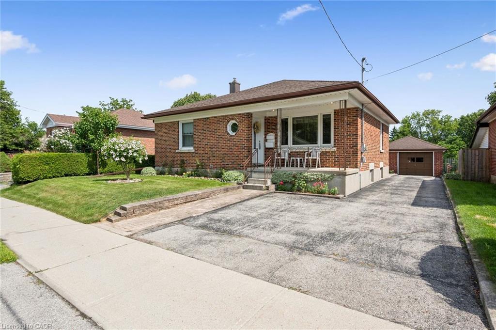 Charming brick ranch featuring a covered front porch, large picture window, and manicured lawn with mature landscaping