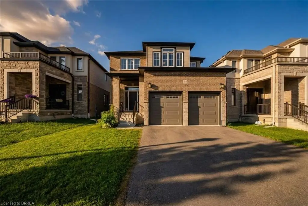 Contemporary exterior featuring a brick facade, stone accents, two-car garage, paved driveway, and manicured front lawn