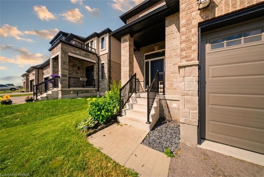 Contemporary exterior featuring brick and stone cladding, an integrated garage, a covered front porch, and a paved walkway
