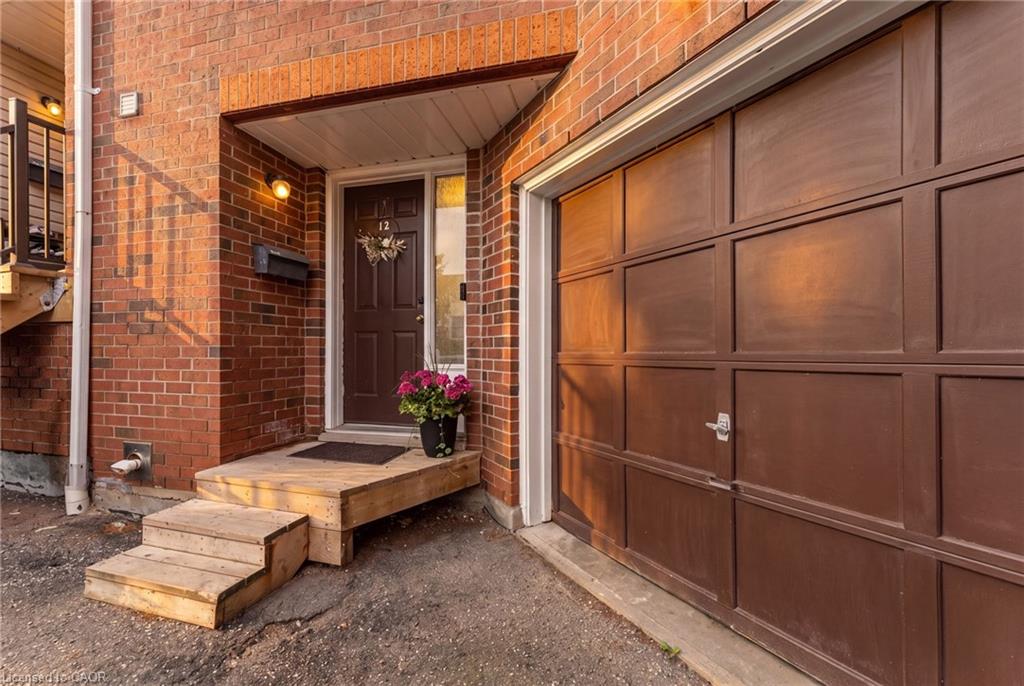 Brick exterior with an attached garage featuring a panel door, wooden steps leading to the main entrance, and an outdoor wall light fixture
