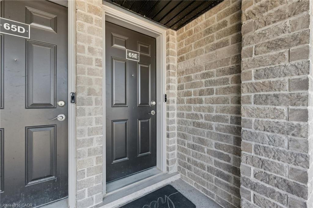 Brick facade entry with a dark panel door and door number 65E