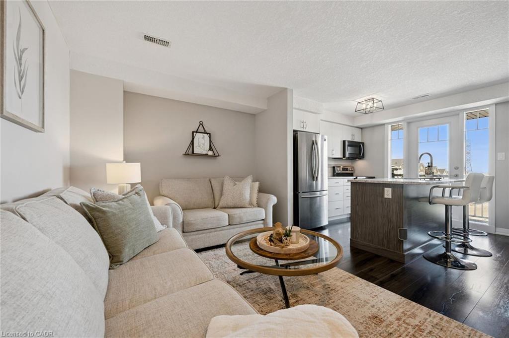 Open-concept living space featuring dark wood-finish flooring, a kitchen island with seating, stainless steel appliances, white cabinetry, and French doors
