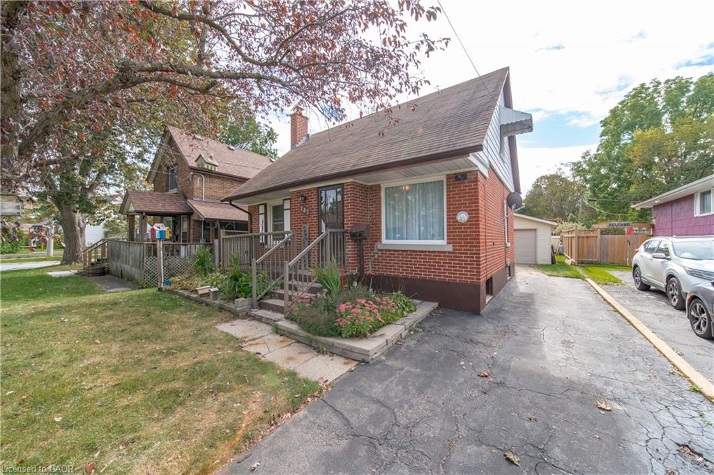 Brick exterior with a peaked roofline, front steps with railings, and a paved driveway. There is also a detached 1.5 car garage/workshop.
