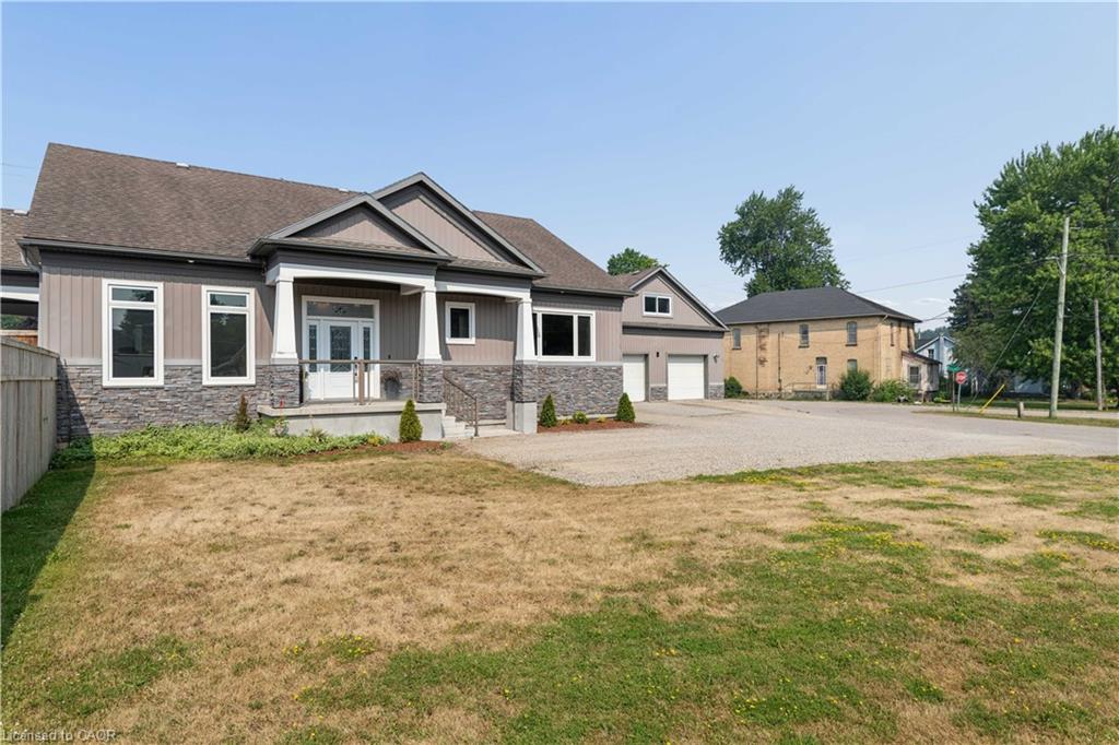 Contemporary exterior featuring a covered entry, stone veneer accents, multiple large windows, a double garage, and a gravel driveway