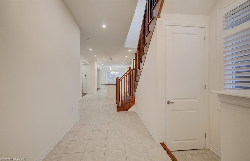 Tiled flooring entrance with recessed lighting, hardwood staircase with wood balusters, and a solid white door