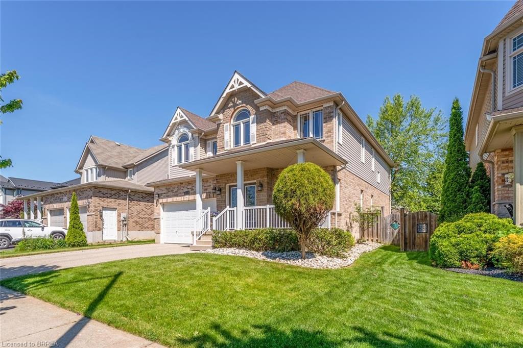 Brick and siding exterior featuring a covered front porch with white railings, arched windows, an attached single-car garage, and a lush front lawn with mature landscaping