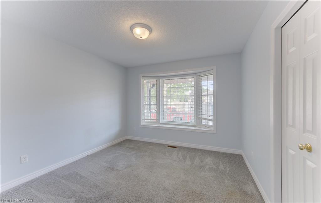 2nd Main Floor Bedroom featuring bay window with blinds, light gray wall paint, gray carpeting, white trim, and a ceiling-mounted light fixture and closet.