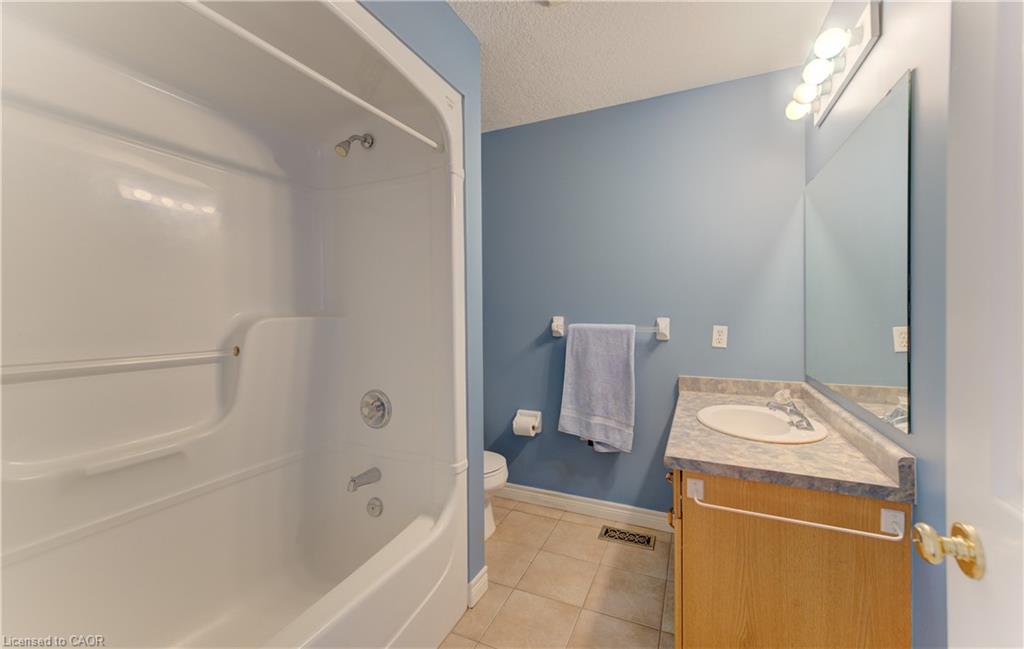 White shower/tub combination with chrome fixtures, wood-finish vanity with an integrated sink, patterned countertop, and a large mirror with overhead vanity lighting
