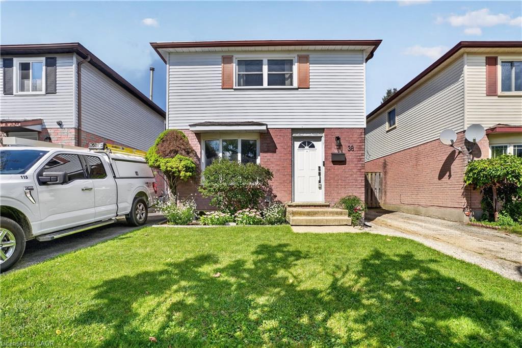 Brick and siding exterior with a concrete pathway leading to the front door, a verdant lawn, and mature landscaping