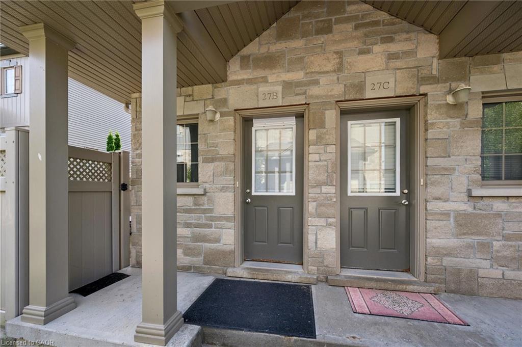 Stone veneer facade, covered porch with pillars, two entry doors with glass inserts, exterior wall sconces, and a side gate