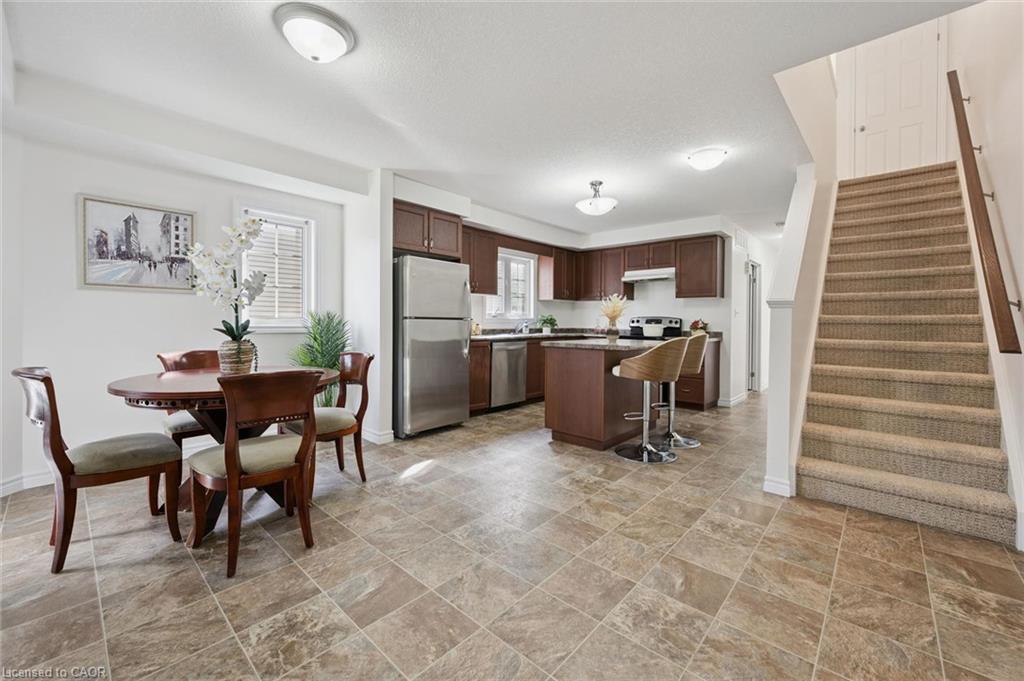 Open-concept living space with tiled flooring, a kitchen featuring dark wood cabinetry and stainless steel appliances, a kitchen island with seating, and a carpeted staircase