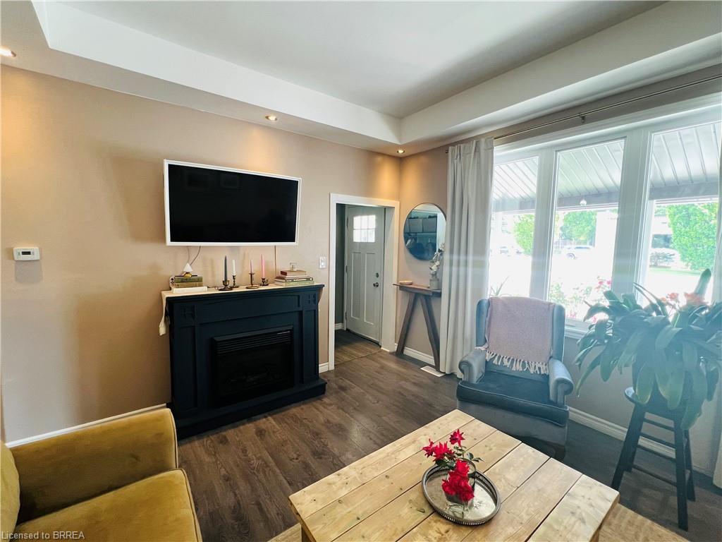 Spacious living area featuring wood-finish flooring, a decorative fireplace, large windows with natural light, a ceiling with recessed lighting, and a front entry door with glass panels
