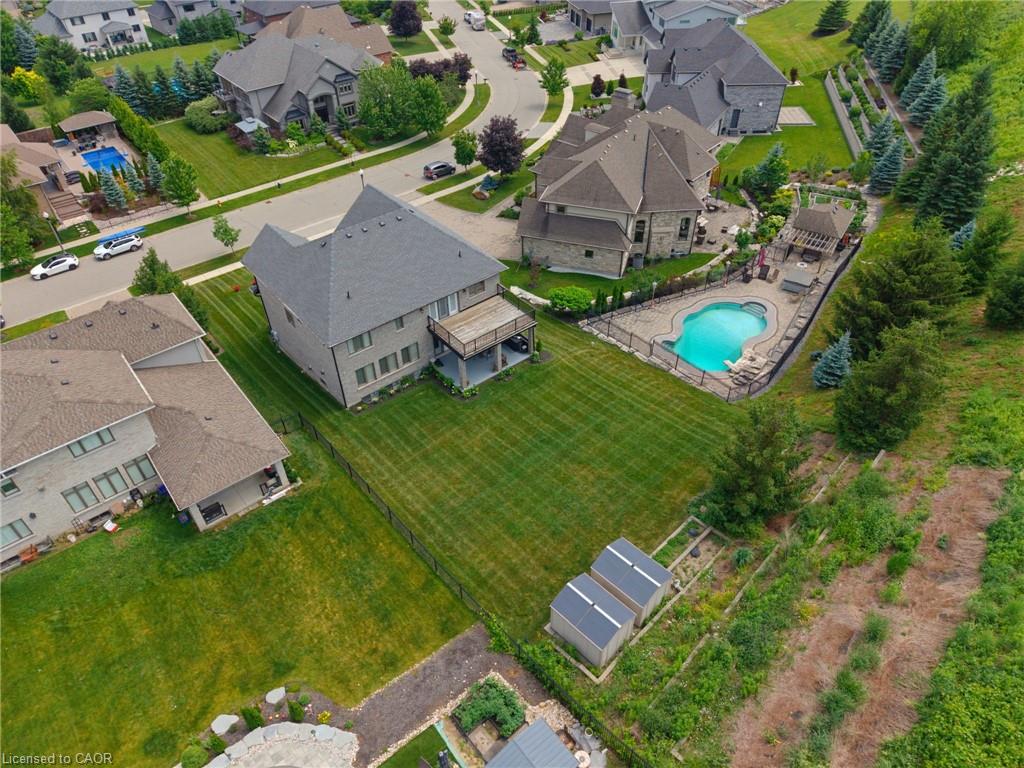 Aerial perspective showcasing a spacious property featuring a private swimming pool with stone surround, an outdoor living area with a pergola, a manicured lawn, and two garden sheds