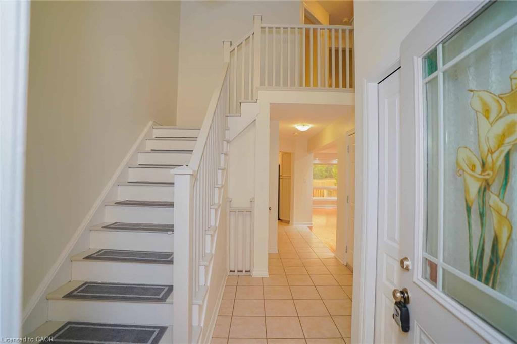 Two-story foyer featuring a white painted staircase with wood banister, second-story open railing, and light-toned tile flooring