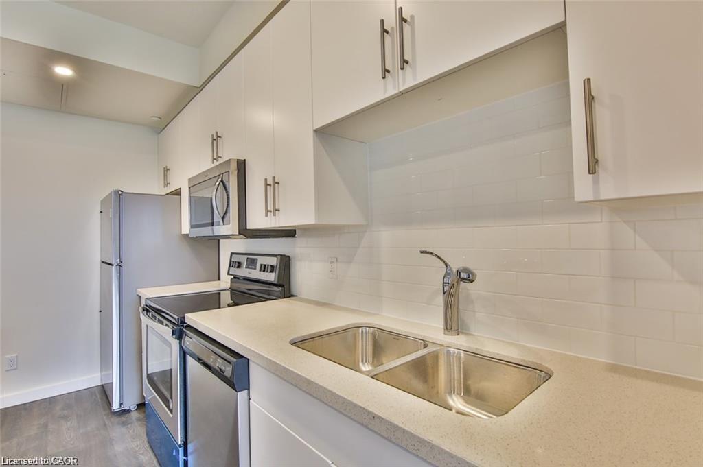 Kitchen featuring stainless steel appliances, white cabinetry, light stone countertops, backsplash, and wood finished floors